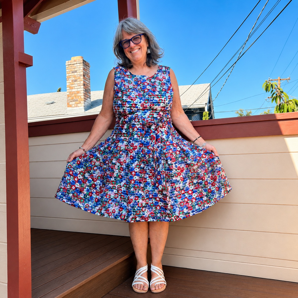 Aunty Anie smiling on a sunlit porch at Canticle Farm in Oakland, holding out the skirt of a floral dress